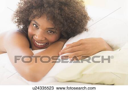 Stock Image - Portrait of woman lying on bed. Fotosearch