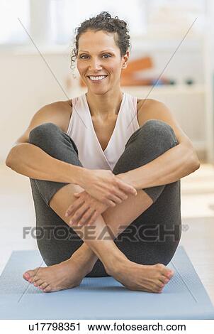 Stock Image - Portrait of woman sitting on exercising mat. Fotosearch