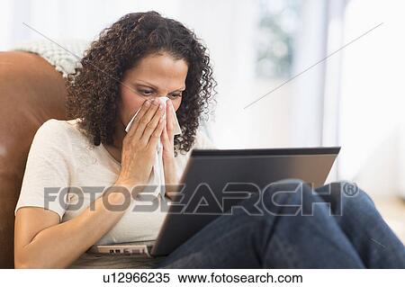 Stock Photography - Portrait of woman sitting with laptop and blowing nose. Fotosearch