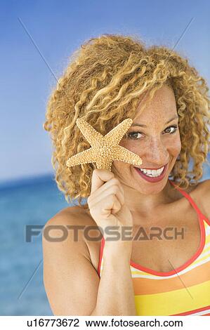 Stock Image - Portrait of young woman holding starfish. Fotosearch
