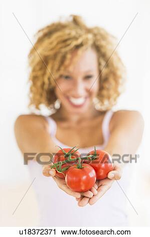 Stock Image - Portrait of young woman holding tomatoes. Fotosearch