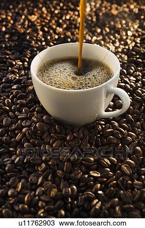 Stock Image - Pouring coffee into cup on coffee beans, studio shot. Fotosearch