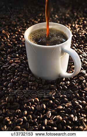Stock Image - Pouring coffee into cup on coffee beans, studio shot. Fotosearch