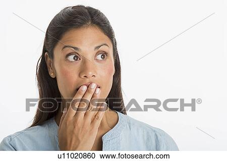 Stock Image - Studio shot of woman covering mouth with hand. Fotosearch