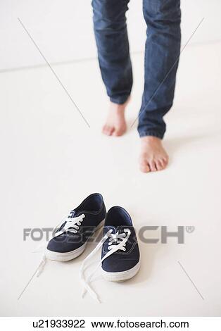 Stock Image - Studio shot of young barefoot woman standing next to shoes, low section. Fotosearch