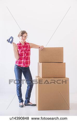 Stock Photo - Studio shot of young woman with tape and stack of boxes. Fotosearch