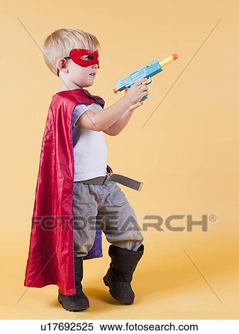 Stock Photography - Studio shot, Portrait of boy (2-5 years) wearing cape and holding toy gun. Fotosearch