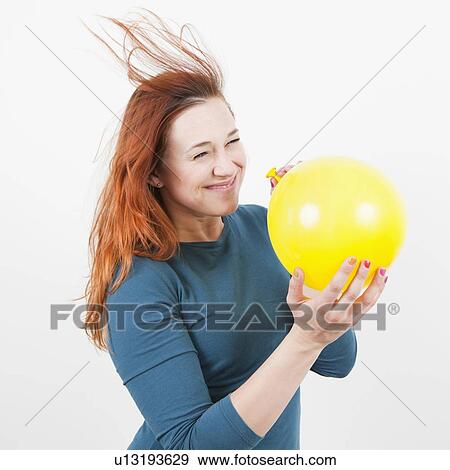 Stock Photo - Studio Shot, Portrait of woman holding yellow balloon and letting air out of it. Fotosearch