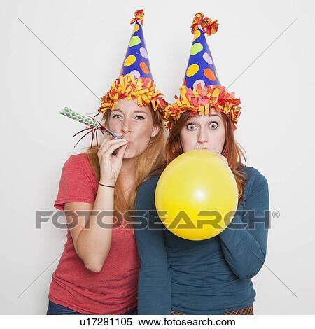 Studio Shot, Two women wearing party hats and one blowing up yellow balloon View Large Photo Image Stock Photography - Studio Shot, Two women wearing party hats and one blowing up yellow balloon. Fotosearch