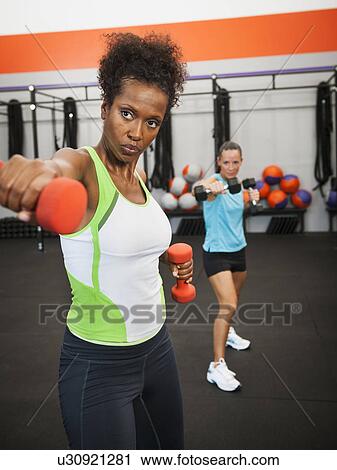 Stock Image - Two mid adult women exercising with dumbbells. Fotosearch