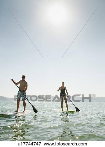 Stock Photo - Two people standing on paddleboard. Fotosearch