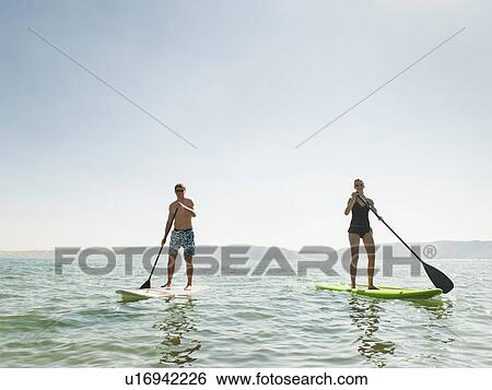 Stock Photograph - Two people standing on paddleboard. Fotosearch