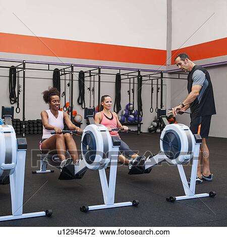 Two women exercising in gym supervised by their trainer View Large Photo Image Stock Image - Two women exercising in gym supervised by their trainer. Fotosearch