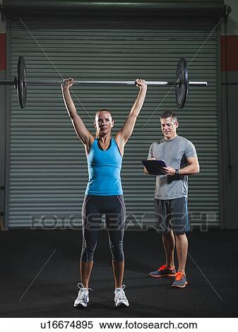 Stock Photography - woman lifting barbell supervised with her trainer. Fotosearch