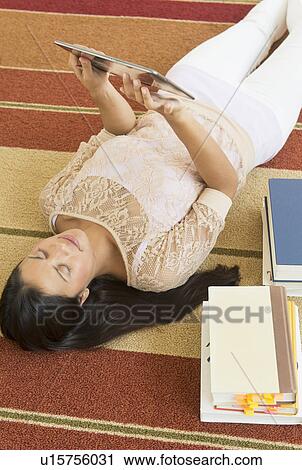 Stock Image - Woman lying on floor and using tablet PC. Fotosearch