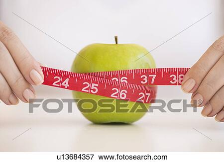 Stock Photo - Woman measuring green apple. Fotosearch