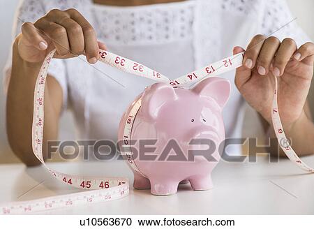 Stock Image - Woman measuring piggy bank. Fotosearch