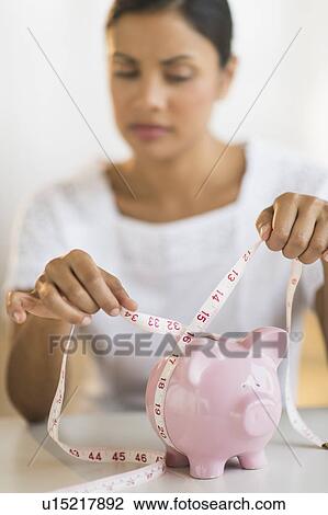 Stock Image - Woman measuring piggy bank. Fotosearch