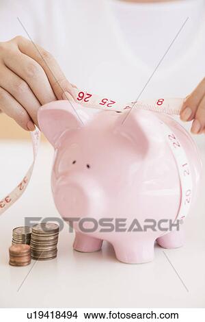 Picture - Woman measuring piggybank. Fotosearch