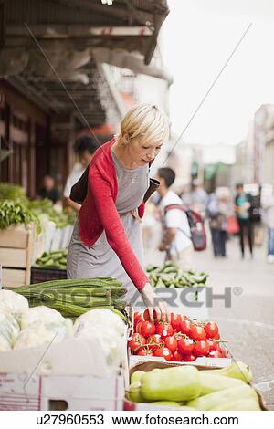 Stock Image - Woman pickig up fresh tomatoes at street market. Fotosearch
