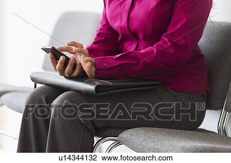 Stock Image - Woman sitting in waiting room and text messaging. Fotosearch