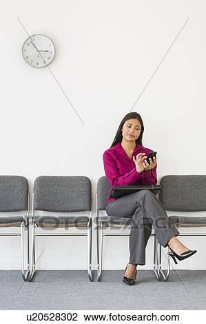 Stock Image - Woman sitting in waiting room and text messaging. Fotosearch