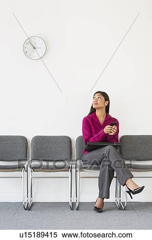 Stock Photography - Woman sitting in waiting room and text messaging. Fotosearch