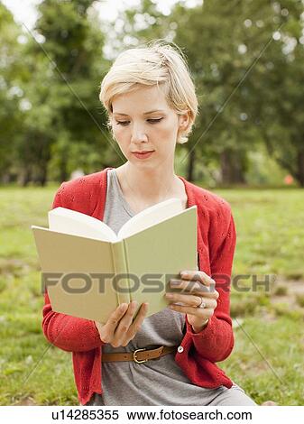 Stock Photography - Woman sitting on grass in park reading book. Fotosearch