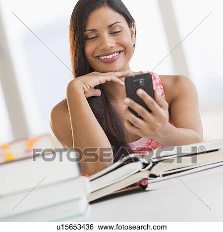 Stock Photograph - Woman text messaging while studying. Fotosearch