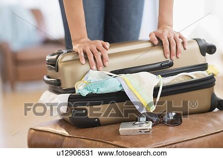 Stock Image - Woman trying to close full suitcase. Fotosearch