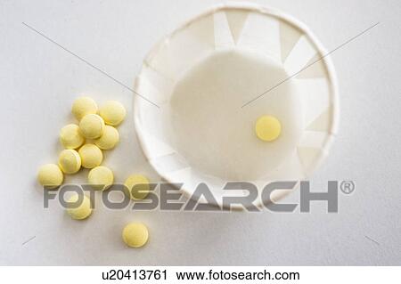 Stock Image - Yellow pills with cup, studio shot. Fotosearch