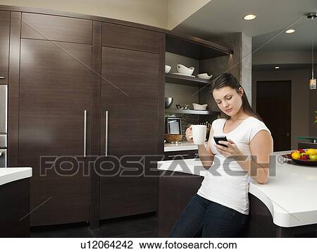 Young attractive woman enjoying morning cup of coffee while checking messages on her mobile phone View Large Photo Image Stock Image - Young attractive woman enjoying morning cup of coffee while checking messages on her mobile phone. Fotosearch
