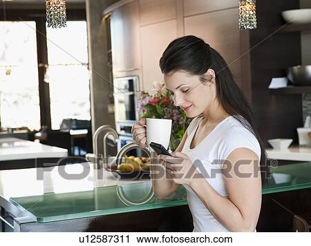 Young attractive woman enjoying morning cup of coffee while checking messages on her mobile phone View Large Photo Image Stock Image - Young attractive woman enjoying morning cup of coffee while checking messages on her mobile phone. Fotosearch