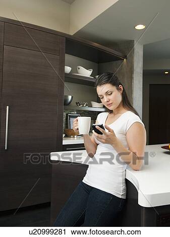 Young attractive woman enjoying morning cup of coffee while checking messages on her mobile phone View Large Photo Image Stock Image - Young attractive woman enjoying morning cup of coffee while checking messages on her mobile phone. Fotosearch