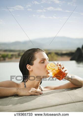Stock Image - Young attractive woman enjoying cocktail on edge of swimming pool. Fotosearch