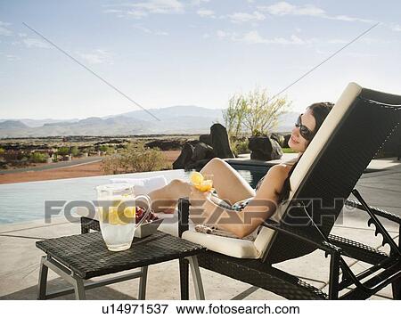 Stock Photo - Young attractive woman enjoying cocktail by swimming pool. Fotosearch