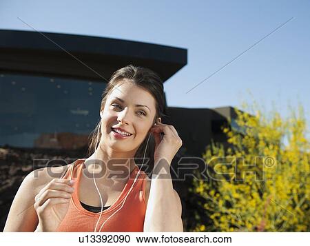 Stock Image - Young attractive woman plugging earphones in her ears. Fotosearch