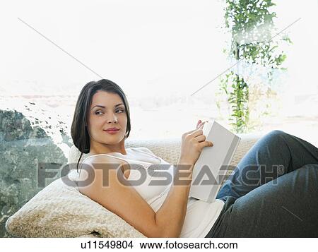 Young attractive woman reading book while sitting on sofa View Large Photo Image Picture - Young attractive woman reading book while sitting on sofa. Fotosearch