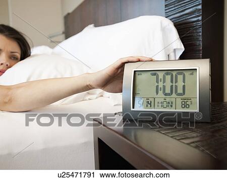 Stock Image - Young attractive woman turning off alarm clock. Fotosearch