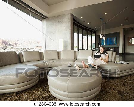 Stock Photograph - Young attractive woman using digital tablet while sitting in her living room. Fotosearch