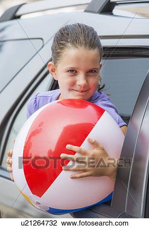 Young girl (8-9) with beach ball peeking through car window View Large Photo Image Stock Image - Young girl (8-9) with beach ball peeking through car window . Fotosearch
