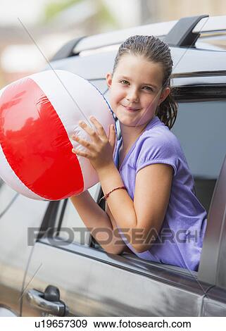 Stock Photo - Young girl (8-9) with beach ball peeking through car window . Fotosearch