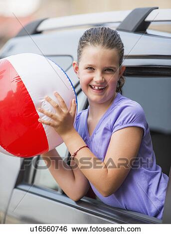 Stock Photograph - Young girl (8-9) with beach ball peeking through car window . Fotosearch
