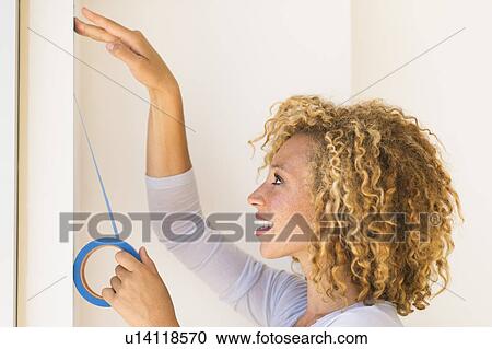 Stock Image - Young woman applying duct tape on wall. Fotosearch