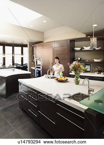 Picture - Young woman bustling around in modern domestic kitchen. Fotosearch