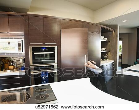 Stock Image - Young woman bustling around in modern domestic kitchen. Fotosearch
