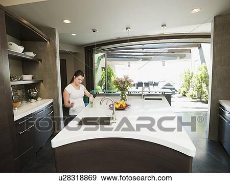 Young woman bustling around in modern domestic kitchen View Large Photo Image Stock Photo - Young woman bustling around in modern domestic kitchen. Fotosearch