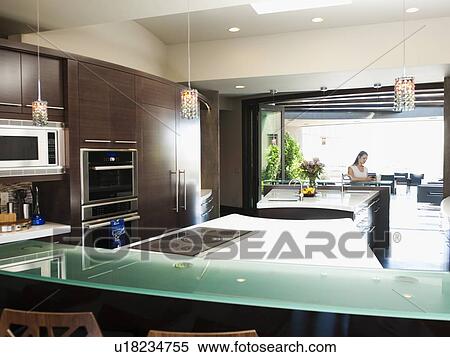 Stock Photography - Young woman bustling around in modern domestic kitchen. Fotosearch