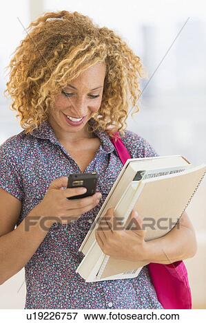 Stock Photo - Young woman carrying books and using mobile phone. Fotosearch