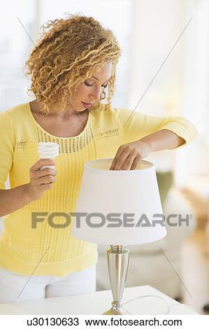 Stock Image - Young woman changing bulb in lamp. Fotosearch